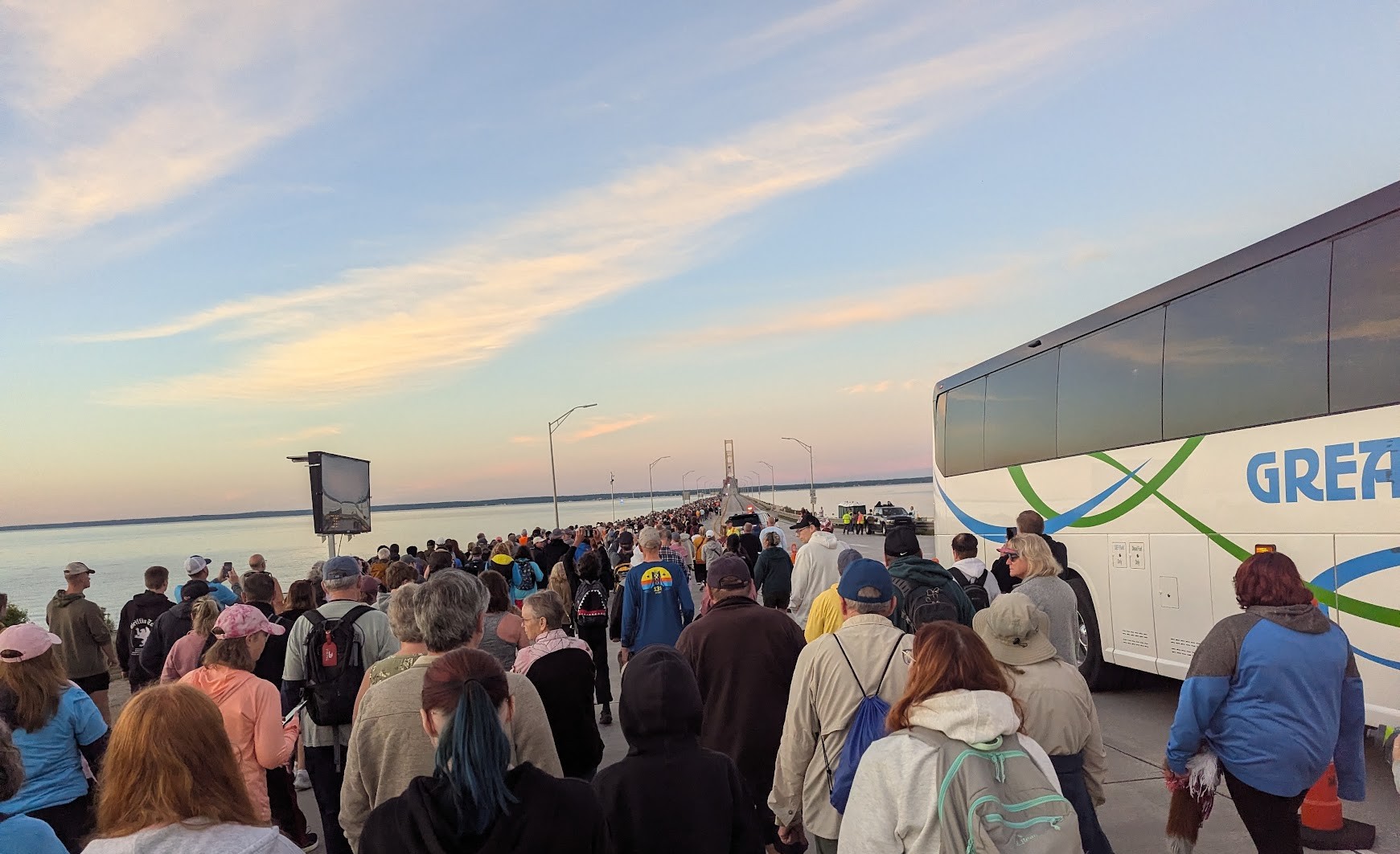 A large crowd walking south from the nortern end of the Mackinac Bridge. The bridge's towers are visible in the distance.
