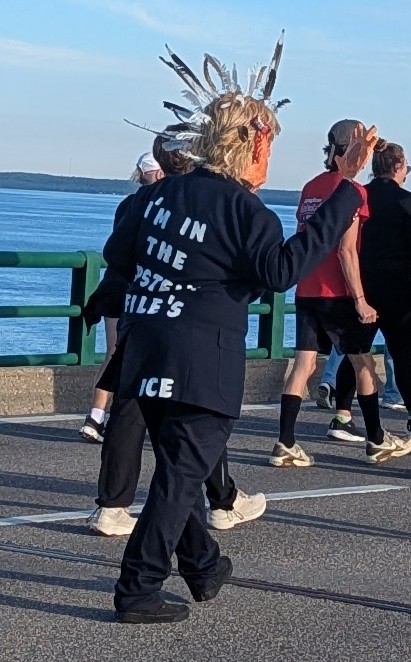 A man wearing a costume intended to make him look like Donald Trump. He is facing away from the camera, with the back of his shirt reading "I'm in the Epstein Files".