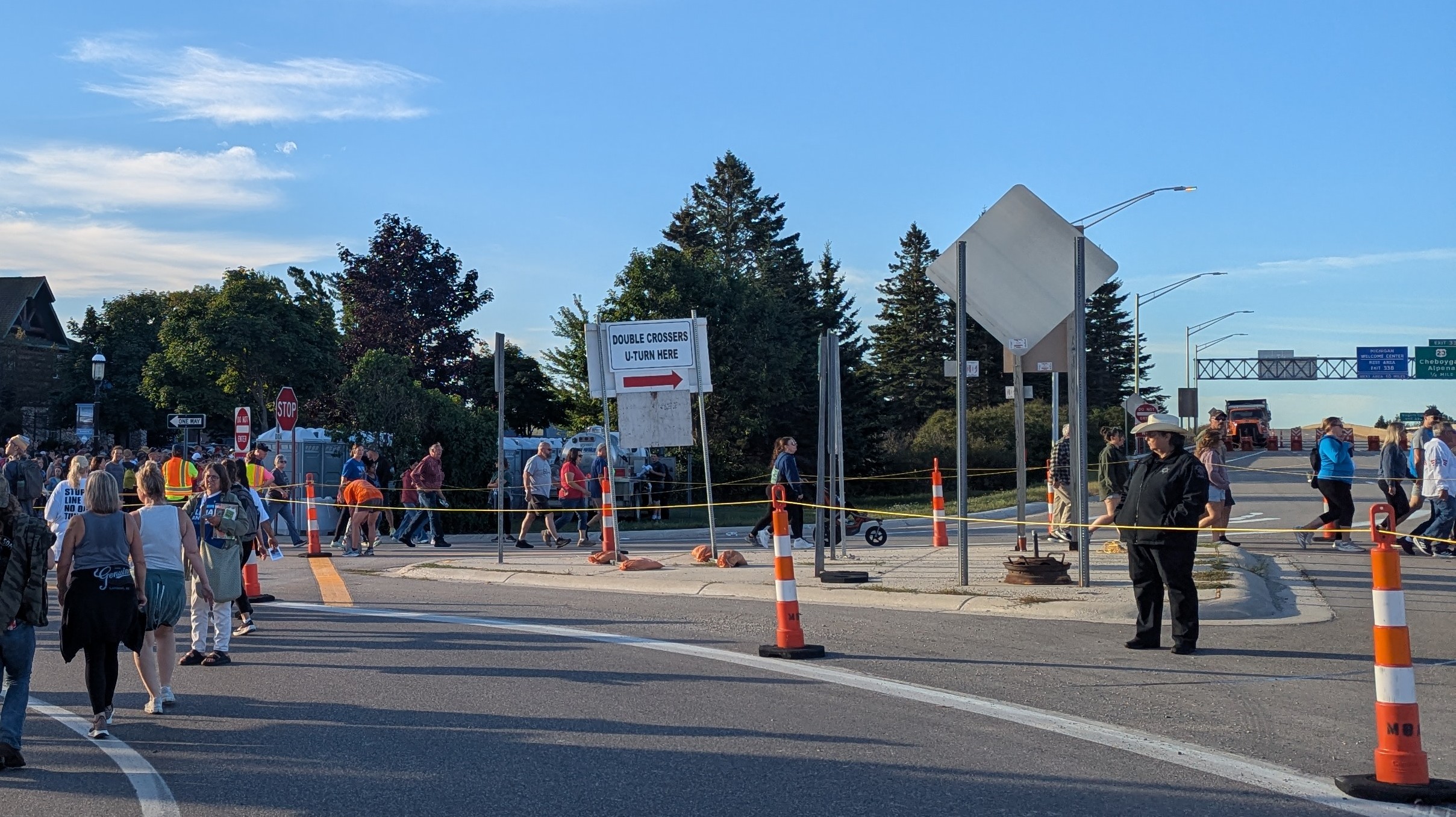 A sign in the center of the frame reads "double crossers U-turn here". People are walking on both sides of the sign.